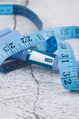 Blue measuring tape and semaglutide injector pens on concrete base, minimalist medical composition for health and pharmaceutical use