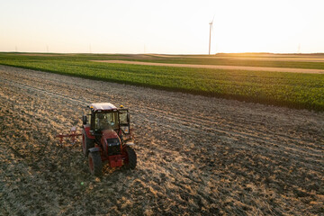 Agricultural tractor is working on the field with wind turbines