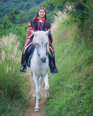 Asian Teen Tourist Girl Enjoys Horseback Riding in Modern Hill Tribe Costume in Chiang Mai, Thailand.