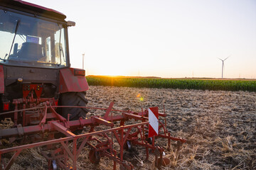 Agricultural tractor is working on the field with wind turbines