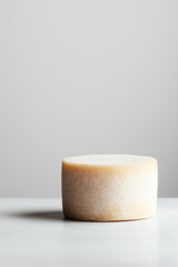 Round cheese wheel resting on a minimalistic surface in a well-lit environment showcasing its smooth texture