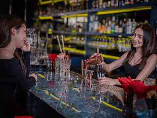 Friendly bartender serving a drink to a smiling female customer in a modern upscale bar. Social nightlife scene, woman enjoying cocktail conversation at a stylish bar counter.