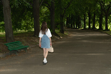 A woman in a casual outfit walks down a tranquil pathway surrounded by trees in a city park....