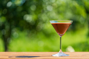 Delicious chocolate martini cocktail served in an elegant glass with a green summer garden...