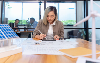 female architect working on blueprint for house with solar roof system, asian woman engineer...