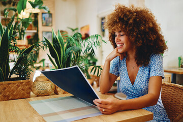 Young woman smiling while choosing meal from menu in a restaurant full of plants
