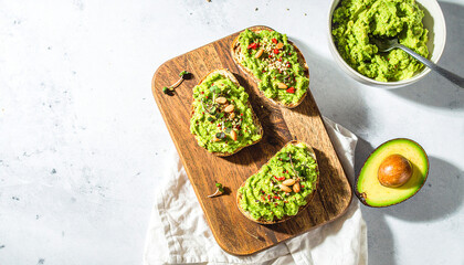 Avocado toast preparation with rustic bread, creamy mashed avocado and fresh garnish on wooden cutting board
