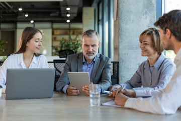 Four business professionals using laptop on desk discussing strategy company