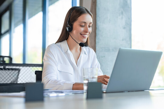 Friendly female helpline operator in call center. Young woman working in call center and holding microphone on headset with hand.