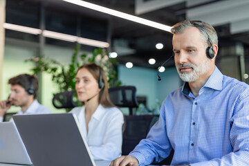Smiling friendly handsome middle aged male call centre operator. Colleagues on the background