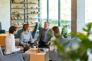 Four business professionals using laptop on desk discussing strategy company