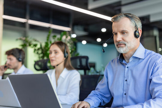 Smiling friendly handsome middle aged male call centre operator. Colleagues on the background - Powered by Adobe