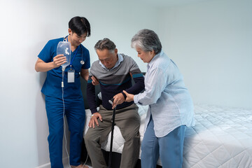 nurse physiotherapist assist support senior man patient with saline infusion to get up from bed....