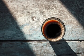 Black Coffee in Glass Cup on Rustic Wooden Surface with Sunlight