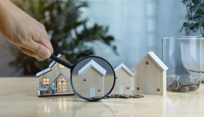 Hand holding magnifying glass over house model. Concept of real estate selection, property...