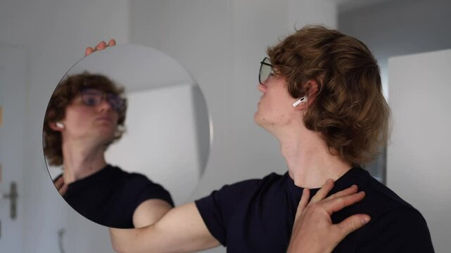 Man holding a round mirror smiles nervously at his own reflection showing visible unease and self-doubt as he examines his face trying to appear confident while hiding discomfort