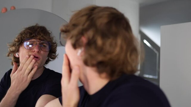 Man makes a disgusted grimace while looking at his reflection in the mirror reacting with visible discomfort and rejection of his own appearance in a moment of self-doubt