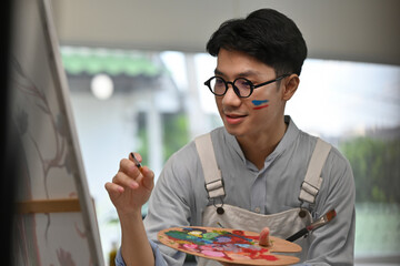 Focused young painter adds detail to his artwork with a steady hand and vibrant colors, expressing...
