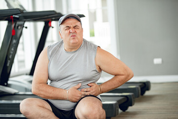 man at the gym with hand on stomach because nausea, painful disease feeling unwell. ache concept.