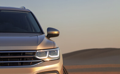 A gray SUV stands parked among the towering sand dunes of the Namib Desert under a dramatic cloudy...