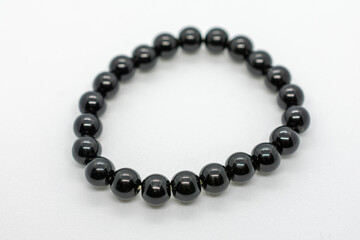 Black bracelet with a shiny surface. The bracelet is made of small black beads. The beads are arranged in a circular pattern. The bracelet is made of a shiny material that reflects light.
