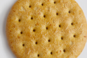 Crunchy round cracker with a golden-brown texture and small holes drizzled with light seasoning on...