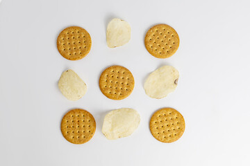 Assorted round crackers and chips arranged in a playful pattern on a white surface during a casual...