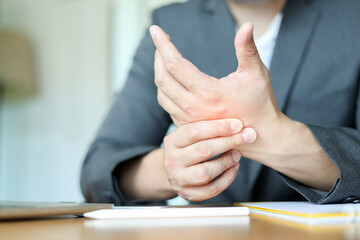 close up employee man massage on his hand and arm for relief pain from hard working on the desktop table at hoe office for stiff or cramp symptom or carpal tunnel syndrome concept