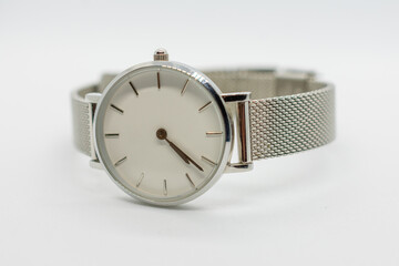 Silver watch with a white face sits on a white background. The watch is simple and elegant, with a...