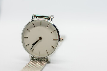 Silver watch with a white face sits on a white background. The watch is simple and elegant, with a...