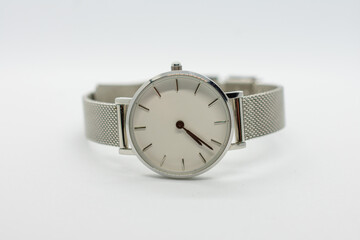 Silver watch with a white face sits on a white background. The watch is simple and elegant, with a...