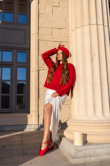 Fashion Model Column: Woman in red sweater posing by pillar, daytime, for artistic portrait...