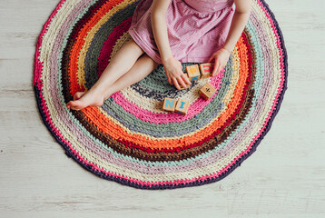 Girl child sit on round colorful crochet rag rug from repurposed T-shirts yarn on white laminate...