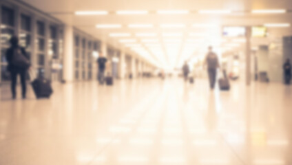 Blurred figures with luggage walking in a bright airport terminal or hallway.