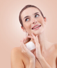 Smiling young woman with makeup holding an plastic jar of face cream near her face while looking...