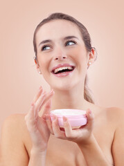 Smiling young woman with makeup holding an open plastic jar of face cream near her face while...