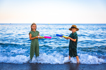 A girl and a boy playing on the seashore with colorful water pistols, splashing water, laughing and...