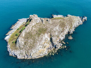 Aerial view of a small rocky island surrounded by clear blue waters, showcasing natural beauty and tranquility. Thacher Rock in Torquay.