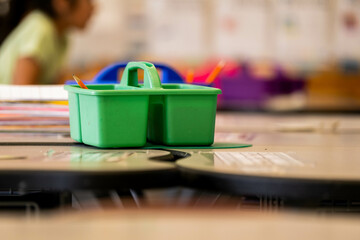 Elementary school desk or small table featuring green supply container with various educational materials and tools. Perfect for back-to-school, organization, and classroom setup content.