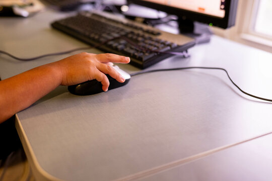 Close-up of student's hand using computer mouse on desk surface with keyboard visible in background. Represents digital learning, computer literacy, and modern educational technology integration