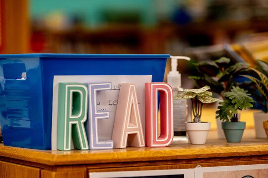 Colorful letter blocks on wooden shelf or teacher desk sell out the word Read, promoting literacy and reading education in a classroom or school library setting