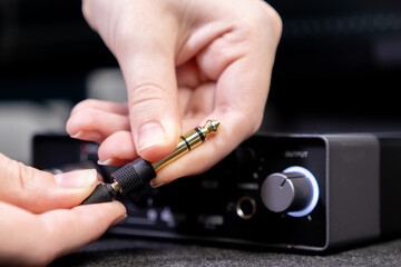 Close-up of human hands precisely plugging a shiny gold-tipped audio jack into a black output port on a professional sound interface for quality music production
