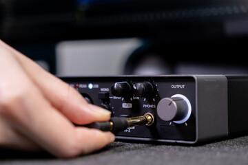 Hand plugging an audio jack into a digital audio interface, illustrating music production and sound...