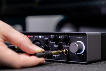 A person's hand plugs a jack cable into the PHONES output of a professional audio interface, essential for music production and sound engineering