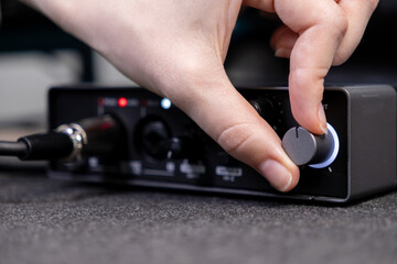 A human hand precisely adjusts the illuminated control knob on a professional audio interface, signifying sound engineering and music production for digital media creation