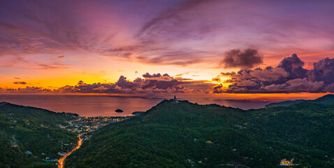 Aerial hyper lapse view of A breathtaking sunset paints the sky in vivid hues of orange and blue over a coastal town, with lush green hills framing the scene. cloud in dramatic sunset over the ocean
