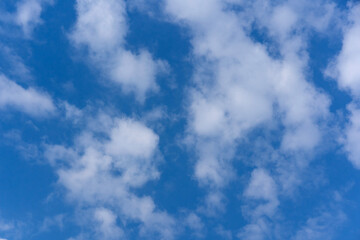 Bright blue sky filled with scattered, fluffy white cumulus clouds on a clear sunny day. Beautiful natural skyscape background for peaceful concepts.