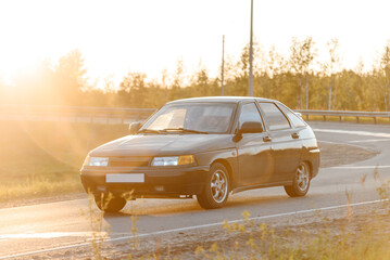 black passenger car driving along road at sunset in summer, transportation and travel concept
