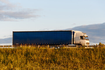 blue and white truck driving along road at sunset in summer, transportation and logistics concept