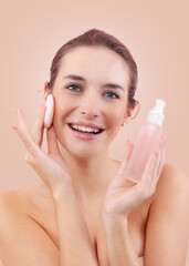 Portrait of a smiling young woman removing makeup with a cotton pad and holding a micellar water...